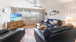 Un salon avec un mur en briques, un meuble en bois, un canapé en cuir noir, une table basse et un téléviseur posé sur un meuble en bois.