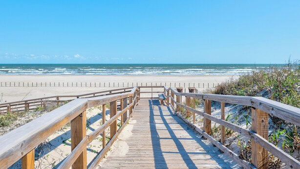 Une promenade en bois qui mène à une plage d’où l’on a une vue dégagée sur l’océan.
