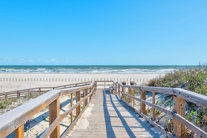 Une promenade en bois qui mène à une plage d’où l’on a une vue dégagée sur l’océan.
