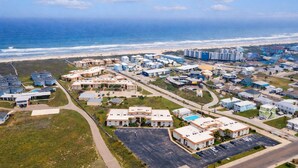 Vue aérienne d’un quartier résidentiel situé sur la côte, avec des propriétés donnant sur la plage, des routes et une plage en arrière-plan.