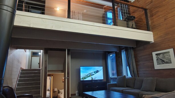 A spacious living area with a large flat-screen TV, a sofa, a coffee table, and a staircase leading to an upper level. - Chilling in the Boat! Location, Comfort & Style (Steamboat Springs)