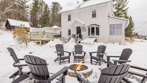 Una casa blanca con un brasero y cuatro sillas Adirondack en la fachada.