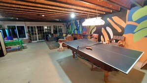 A room with a ping pong table, a sofa, and a colorful mural on the wall.