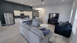 A modern kitchen with a built-in oven and microwave, a grey sofa with patterned cushions, a black sofa, and a flat-screen TV.