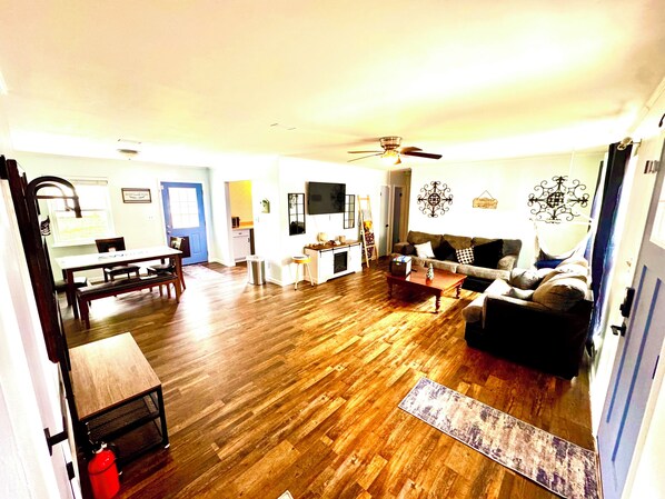 A living room with a wooden floor, a dining area with a table and chairs, a sofa, and a ceiling fan.