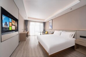Quarto de hotel moderno com uma cama grande, uma escrivaninha, uma televisão e vista para um edifício pela janela.