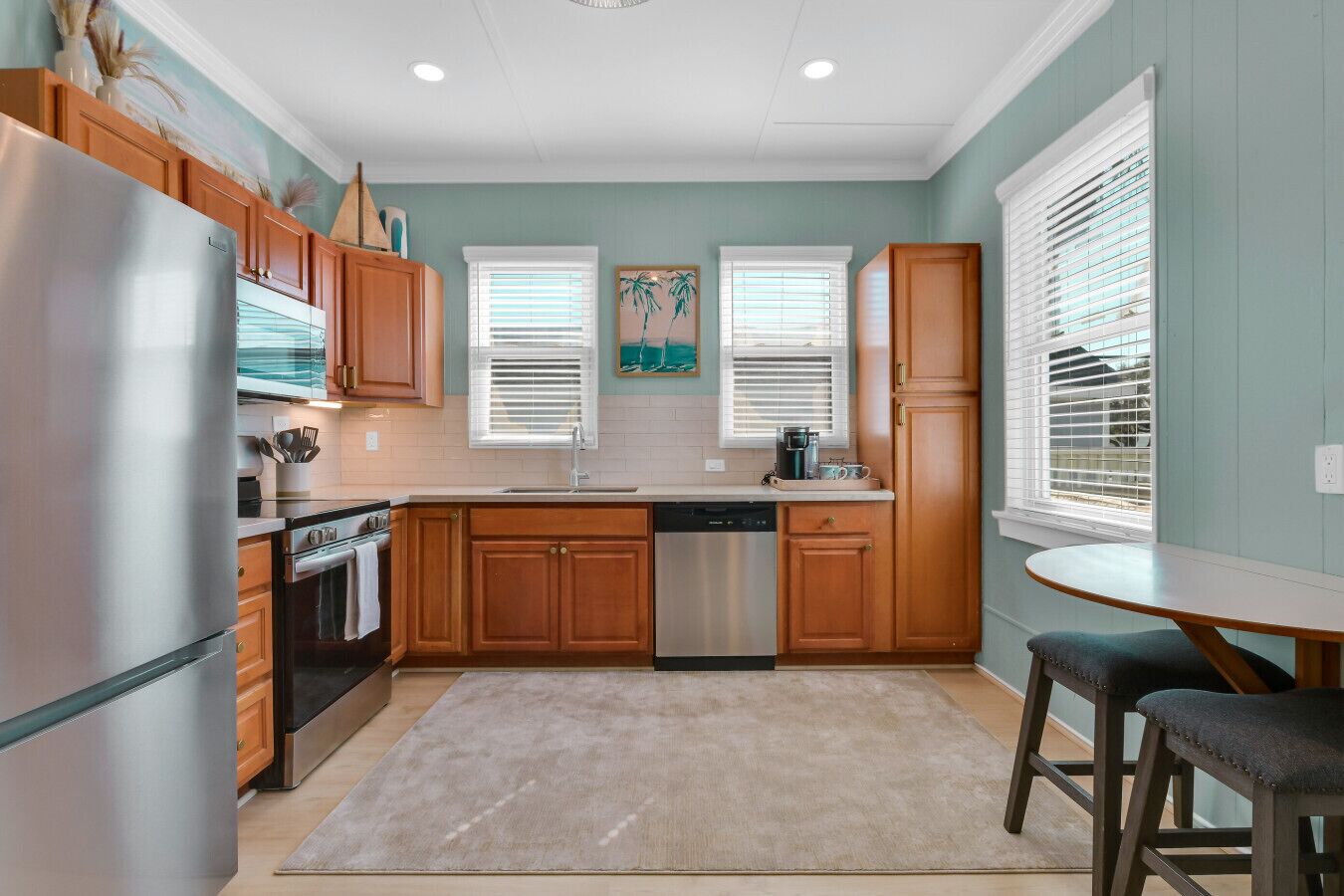 A kitchen with wooden cabinets, a stainless steel refrigerator, a dishwasher, and a dining area with a table and chairs.