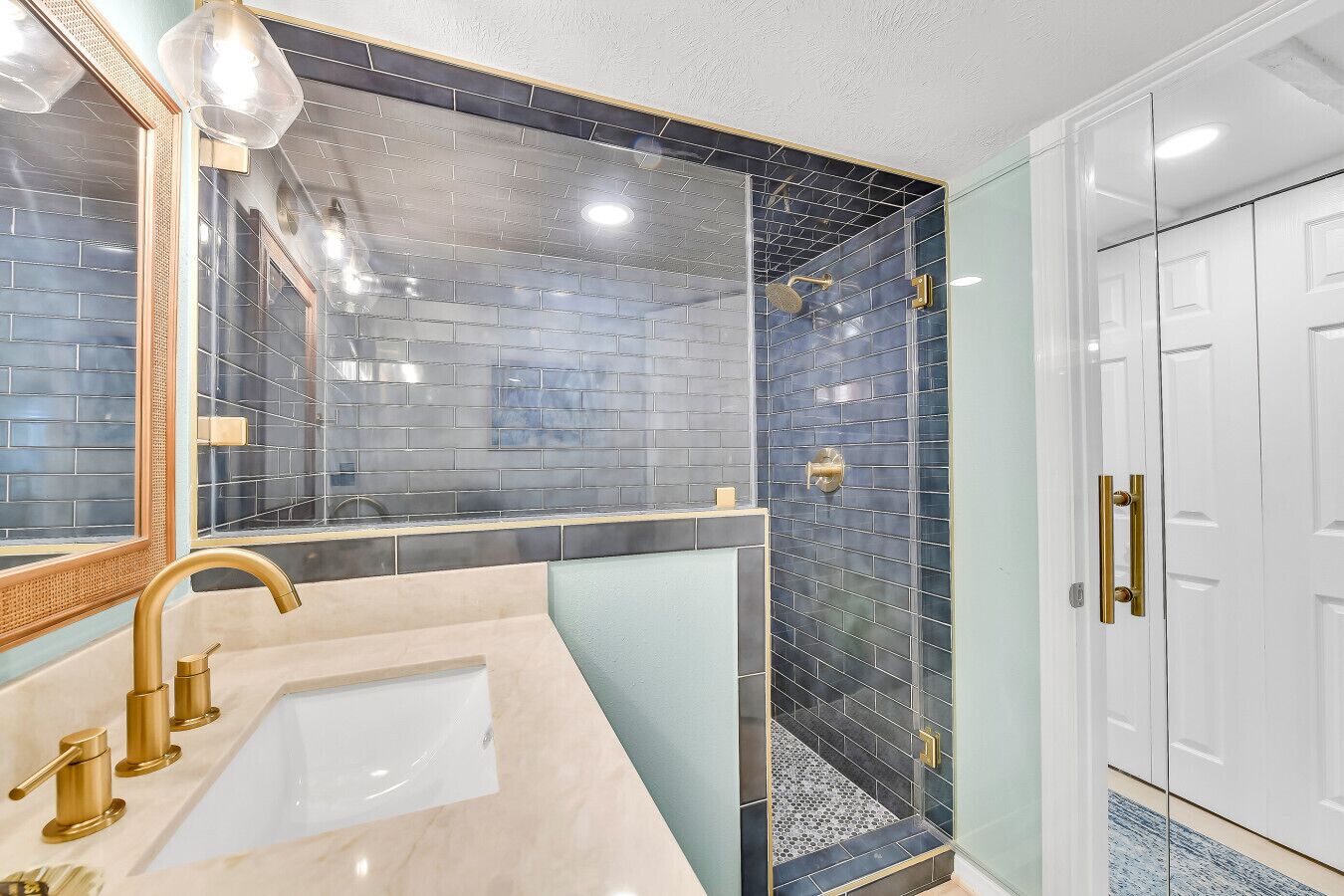 A bathroom with a sink, mirror, and shower area with tiled walls.