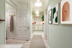 A hallway with a door, a rug, and a kitchen in the background.