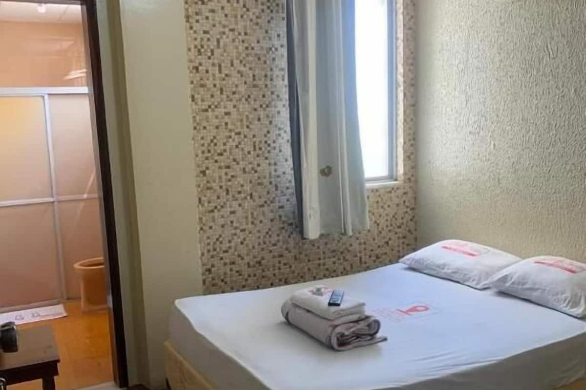 A small, neatly arranged bedroom with a single bed, a bedside table, and a window with curtains.