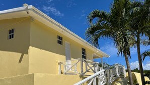 A yellow building with a white staircase leading to a door, surrounded by palm trees. - Coral Cottage Cove-Amazing Ocean Views - 3 Bedroom 2 Bath in St. Thomas (St. Thomas)