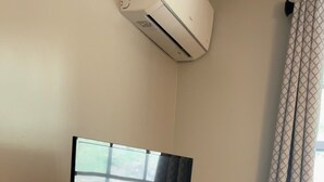 Un televisor de pantalla plana sobre un mueble de madera, una ventana con vistas y una cortina estampada.