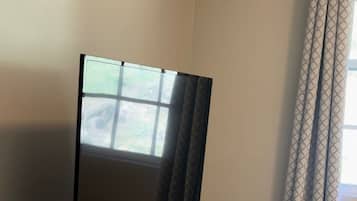 A flat-screen TV on a wooden cabinet, a window with a view, and a patterned curtain.