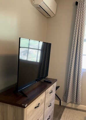 Ein Flachbildfernseher auf einem Holzschrank, ein Fenster mit Aussicht und ein gemustertes Vorhang.