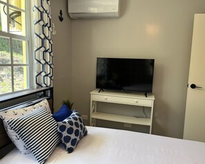 Ein Schlafzimmer mit einem Bett, einem Fernseher auf einem weißen Schrank, einem Fenster mit Vorhängen und einer Tür.