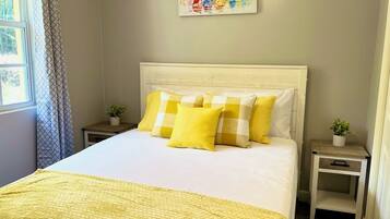 A neatly made bed with a yellow quilt, a white headboard, and matching pillows. There is a painting of sailboats on the wall above the bed.
