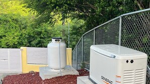 Two Generac generators on concrete bases surrounded by mulch, with a chain-link fence and greenery in the background. - Coral Cottage Cove-Amazing Ocean Views - 3 Bedroom 2 Bath in St. Thomas (St. Thomas)