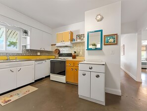 A modern kitchen with white cabinetry, a yellow countertop, and a dishwasher. There is a wooden cabinet with a blue frame above the sink, and a small potted plant on the counter. - Gulfport Getaway — Artsy Retreat 10 Min to Beach (Gulfport)