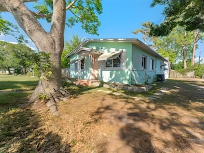 A single-story house with a porch, surrounded by trees and a grassy yard. - Gulfport Getaway — Artsy Retreat 10 Min to Beach (Gulfport)