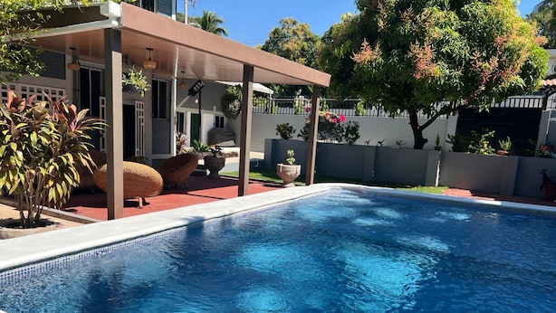 Une piscine dotée d’un patio couvert, entourée de plantes en pot et d’une clôture blanche.