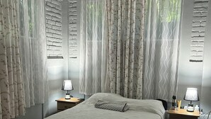 Une chambre à coucher avec un lit, deux tables de chevet avec des lampes, une commode et une fenêtre avec des rideaux.