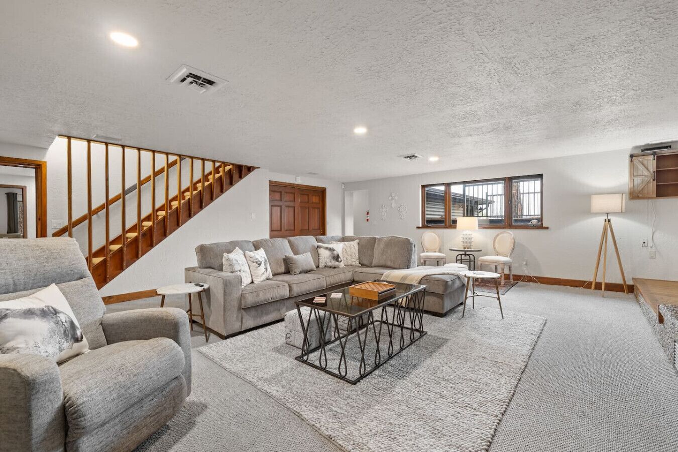 A spacious living room with a grey sectional sofa, a coffee table, and a staircase.
