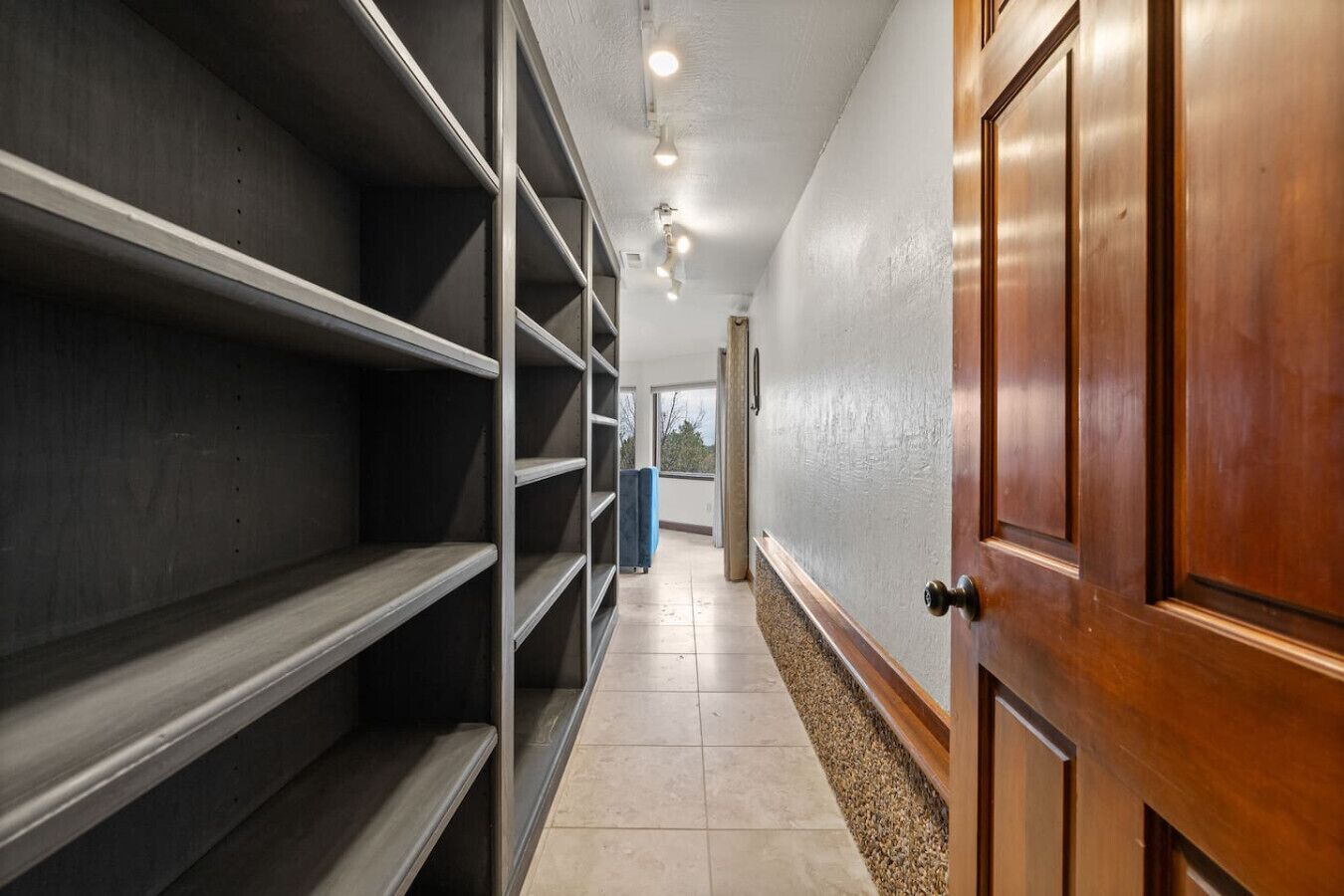 A hallway with metal shelving units, a wooden door, and a tiled floor.