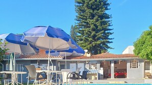 A poolside area with outdoor seating, a covered patio, and a large tree in the background. - Villa Giglio Pousada Atibaia  (Atibaia)