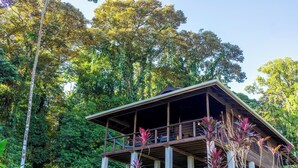 Eine Holzhütte mit Balkon, umgeben von üppigem Grün und Bäumen.