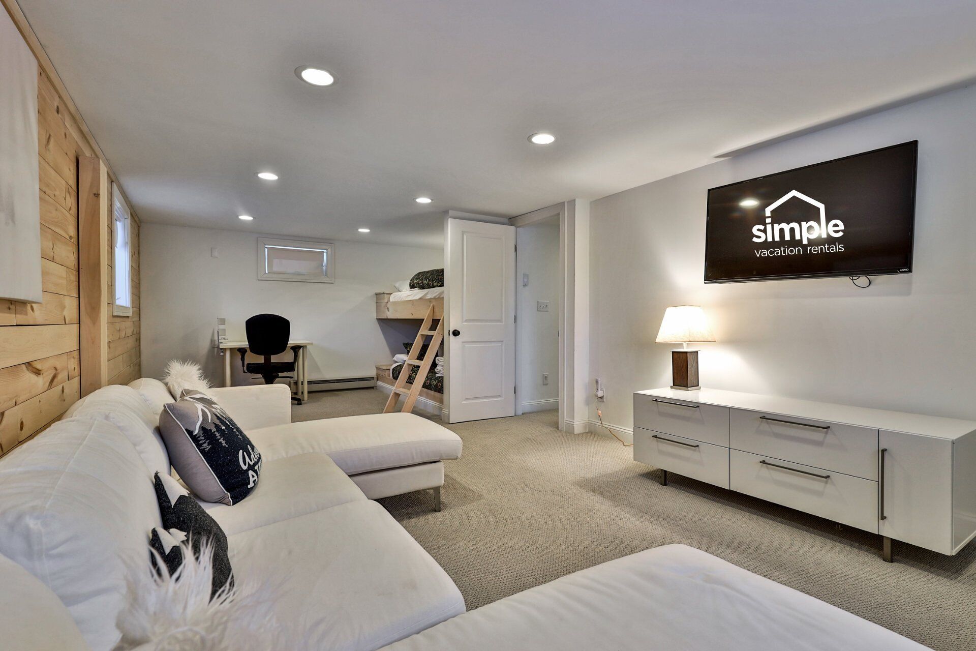 A modern, well-lit bedroom with a bed, a desk, and a TV displaying 'simple vacation rentals'.