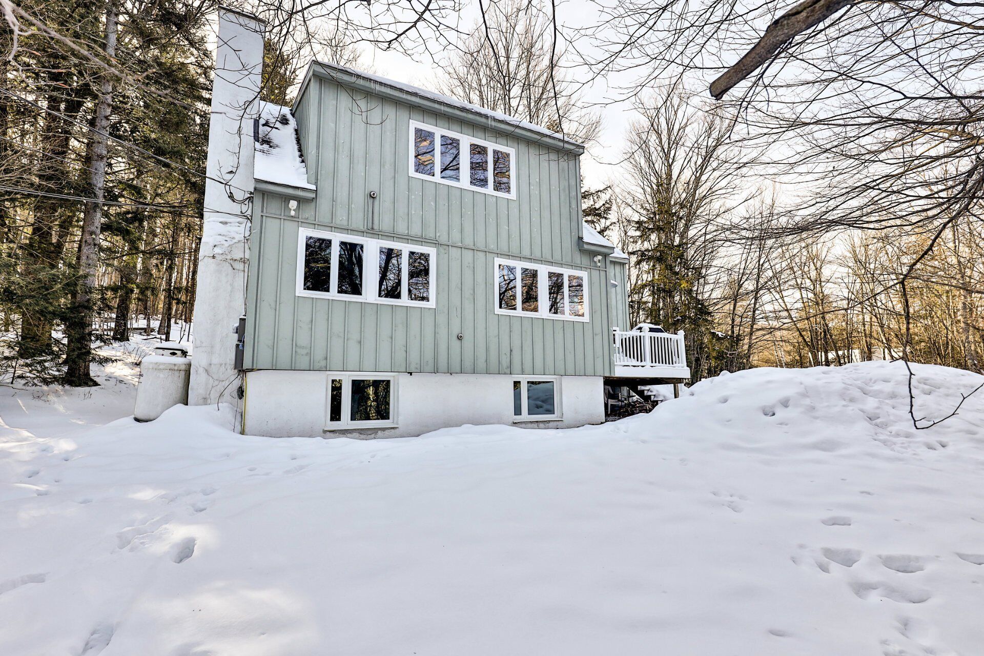 A two-story house with a balcony, surrounded by snow and trees.