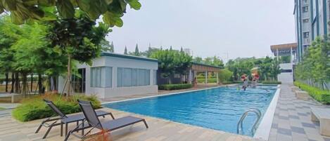 Una piscina con sillas de descanso, un edificio pequeño y un edificio alto al fondo.