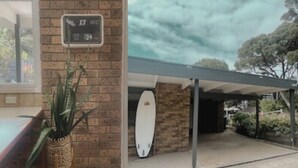 Un bâtiment en briques avec une planche de surf placée sous un espace abrité et un panneau indiquant des numéros.