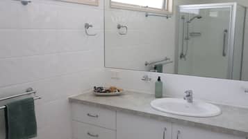 A bathroom with a white sink, a mirror, a towel rack, and a glass shower enclosure.