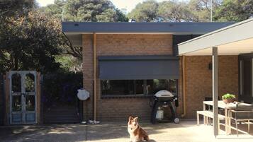 A modern outdoor patio with a barbecue grill, a dog, and a covered seating area.