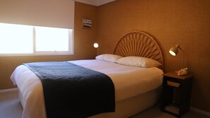 Une chambre à coucher comprenant un lit, une lampe de chevet, une table de chevet, une fenêtre et un tableau accroché au mur.