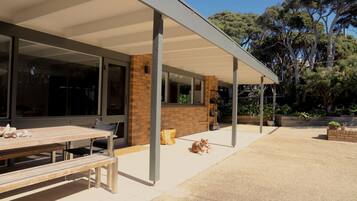 A covered outdoor seating area with a bench, a table, and a dog.