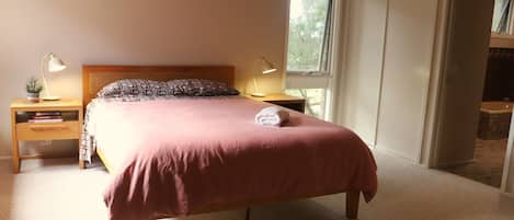 Quarto com cama, abajures, mesa de cabeceira, janela e vista para um banheiro.
