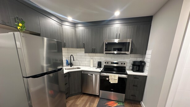 Una cocina moderna con electrodomésticos de acero inoxidable, encimeras blancas y armarios de madera oscura.