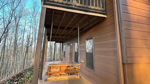 A wooden cabin with a balcony, a wooden deck, and a view of the surrounding forest. - Comfortable Cabin in Hiawassee across from Lake&Fairgrounds (Hiawassee)