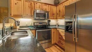 A kitchen with wooden cabinets, stainless steel appliances, a double sink, and a granite countertop. - Comfortable Cabin in Hiawassee across from Lake&Fairgrounds (Hiawassee)