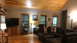 A living room with a wooden ceiling, a television, a sofa, and a lamp. - Comfortable Cabin in Hiawassee across from Lake&Fairgrounds (Hiawassee)
