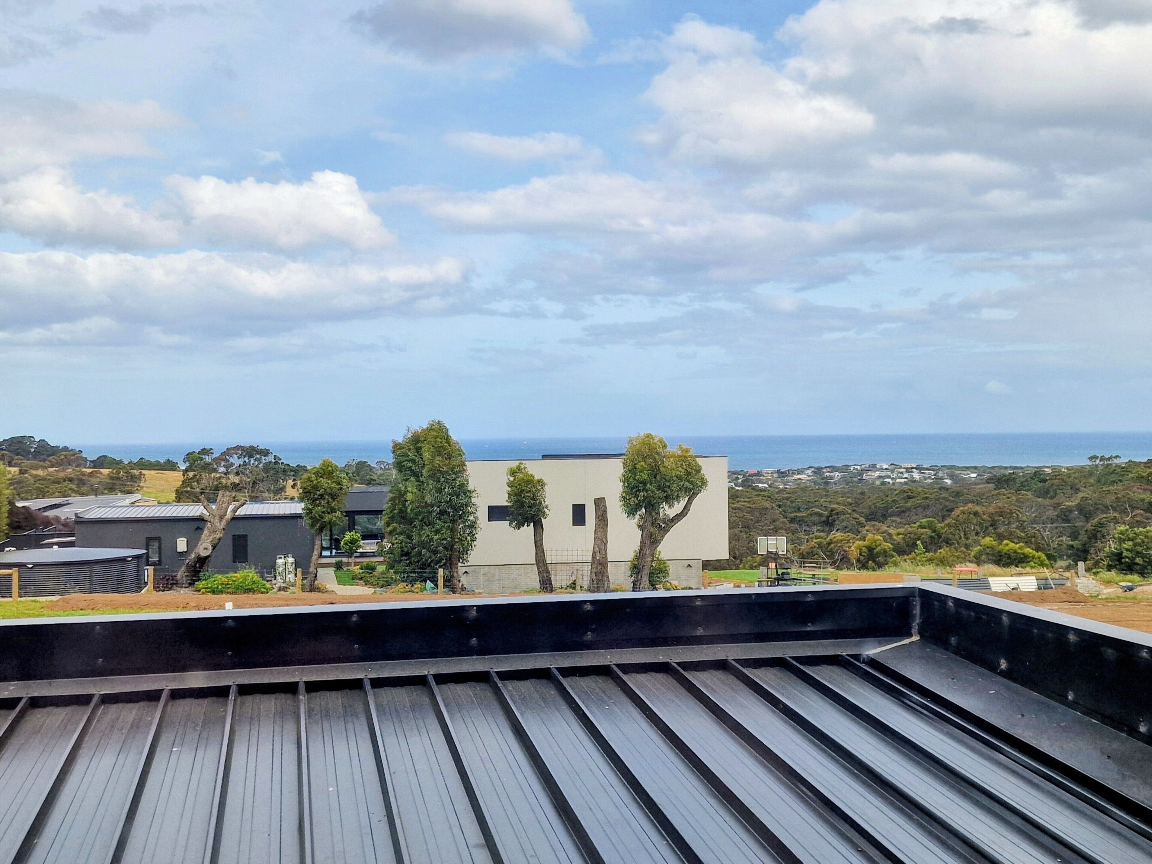 A rooftop with a view of the ocean and a modern building in the distance.