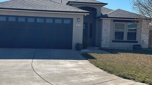 A two-story house with a garage, a stone exterior, and a clear driveway.