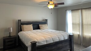 A bedroom with a bed, a nightstand, a ceiling fan, and a window with curtains.