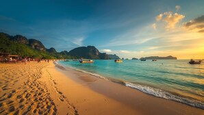 Ein Strand mit klarem türkisblauem Wasser, einem Sandufer und Booten.