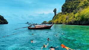 Ein Boot im kühlen, türkisblauen Wasser, während Menschen schwimmen und schnorcheln.