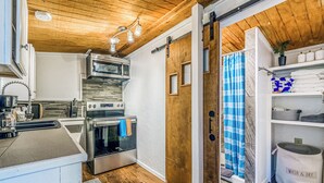 A kitchen with a wooden ceiling, stainless steel appliances, and a sliding door leading to a bathroom with a blue shower curtain. - Mountain Top House with a View - Elk House (Ruidoso)
