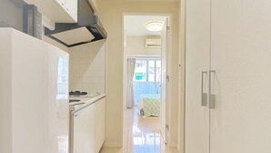 A modern kitchen with white cabinets and a stainless steel range hood. A hallway leads to a bedroom with a bed and a window. - Kinshicho Station, sightseeing area ・Near Tokyo Skytree and Asakusa, sightseeing area ・Direct access to airport (墨田区太平2－9－5)