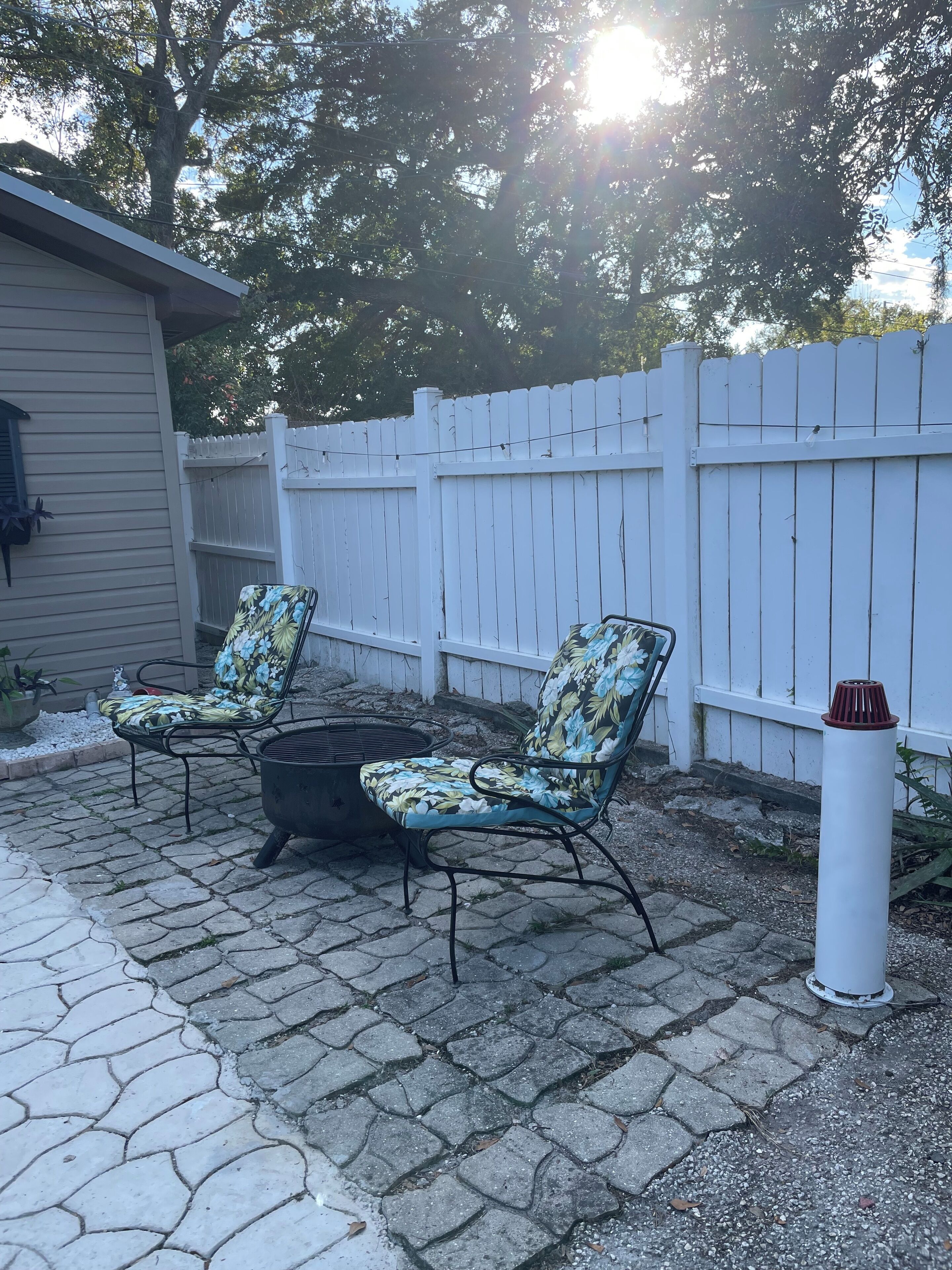 A patio with two chairs and a fire pit, surrounded by a white fence and a house.